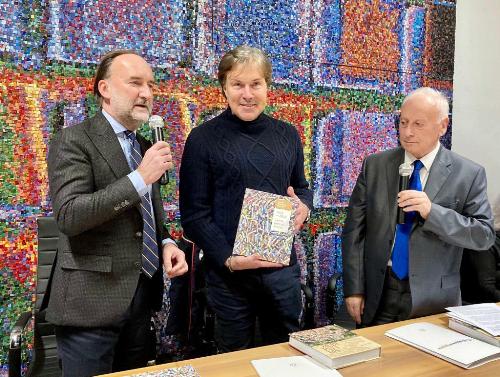 Il libro sui 100 anni della Scuola mosacisti del Friuli donato all'assessore Bini dal presidente dell'istituto spilimberghese Stefano Lovison (a sinistra)