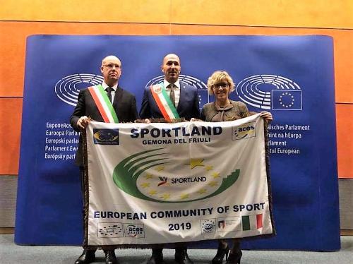 L'assessore regionale Barbara Zilli insieme ai sindaci di Gemona e Buia a Bruxelles con la bandiera ricevuta dai rappresentanti di Aces Europe per il progetto Sportland